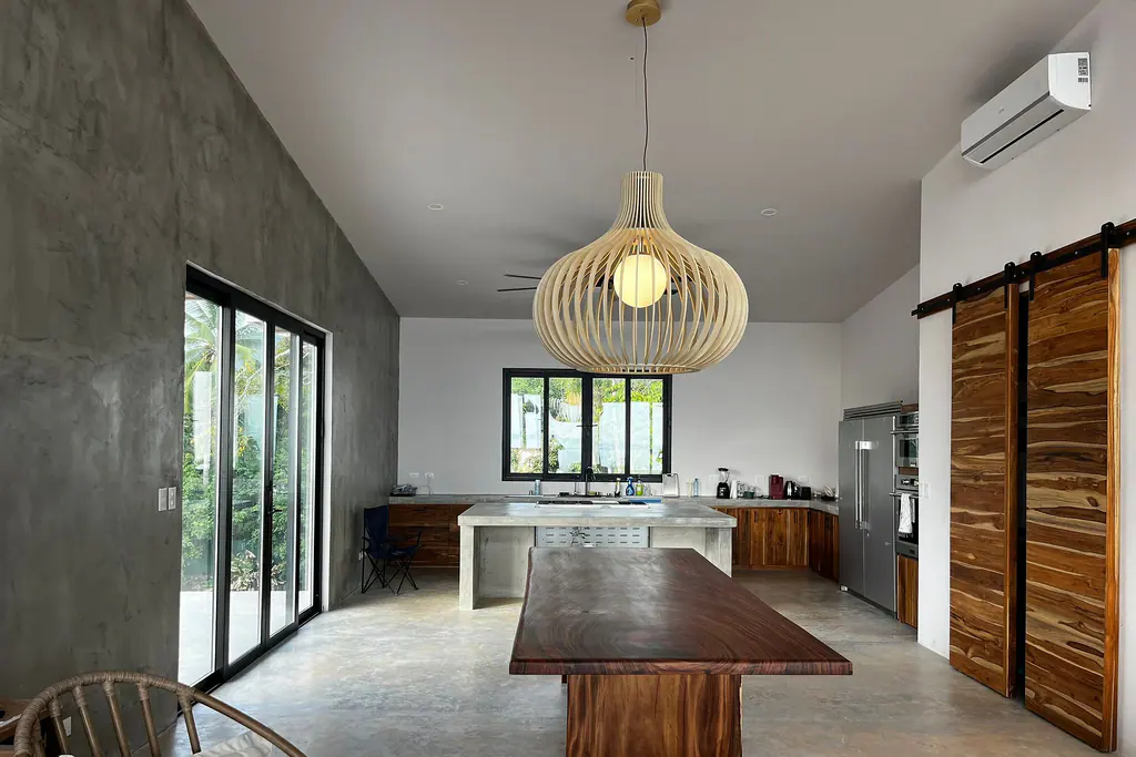 Cocina con isla de concreto, mesa de madera y piso lujado
