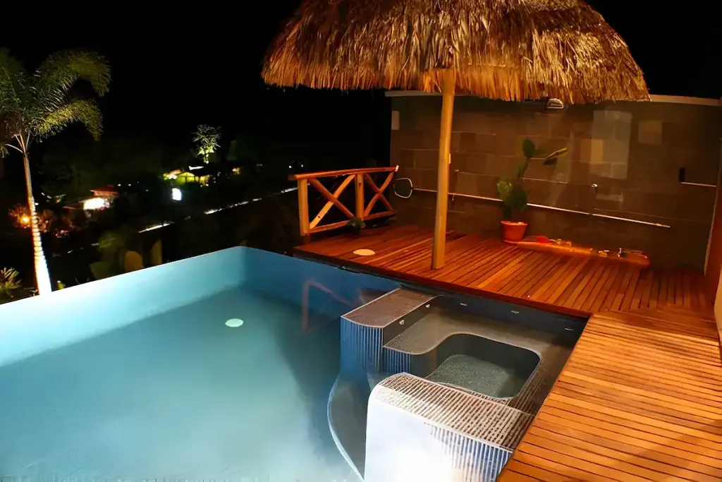 Piscina infinita con deck de madera y rancho, de noche